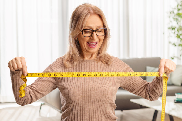 Kobieta uśmiecha się i trzyma miarę krawiecką